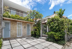 A modern building with a stone facade, a balcony with plants, and a tiled patio area. - Swan Villas in Seminyak (Seminyak)