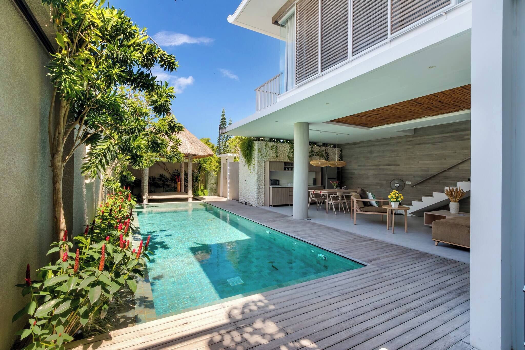 A modern outdoor pool area with a wooden deck, a covered seating area, and a staircase leading to an upper level.