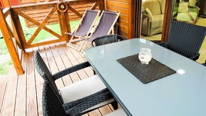 A wooden deck with a glass table and two chairs, a tire swing, and a glass door leading to an indoor area.