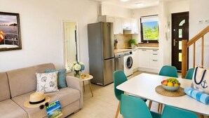 A compact living space with a sofa, dining table, chairs, a refrigerator, a washing machine, and a small kitchen area.