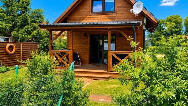 A wooden cabin with a porch, satellite dish, and a fenced yard.