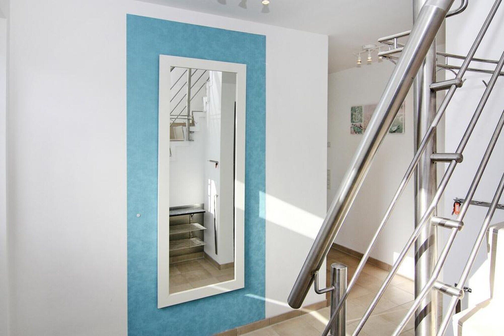 A modern interior with a blue accent wall, a mirrored door, and a metal staircase.