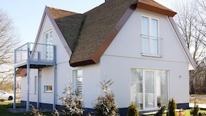 Une maison à deux étages dotée d’un balcon, de grandes fenêtres et d’un toit en pente.