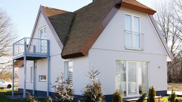 Una casa de dos pisos con balcón, ventanas grandes y techo inclinado.