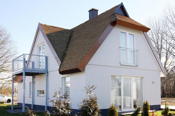 A two-story house with a balcony, large windows, and a sloped roof.