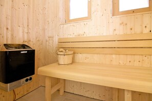 A sauna room with a bench, a Harvia sauna heater, and a wooden bucket.