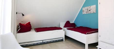 A small, well-lit room with two beds, a white chair, and a cabinet.