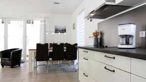 Una cocina moderna con armarios blancos, una cafetera y un comedor con sillas y una mesa.