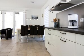 A modern kitchen with white cabinets, a coffee maker, and a dining area with chairs and a table.