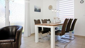 Een eetruimte met een witte tafel, zes stoelen en een moderne klok aan de muur.