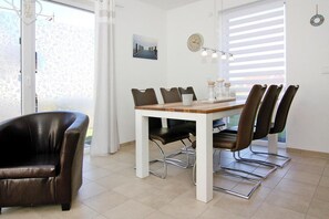 Uma sala de jantar com uma mesa branca, seis cadeiras e um relógio moderno na parede.