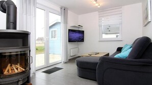 Un salon moderne avec une cheminée, un canapé, un téléviseur et une vue sur l’extérieur.