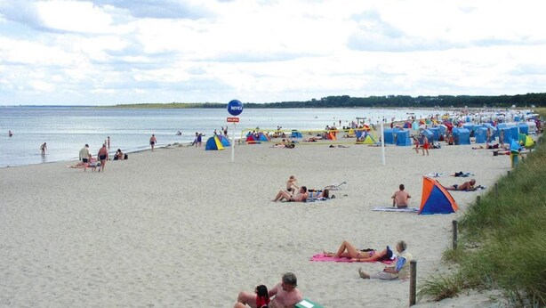 Une plage bondée, avec des tentes et des gens qui prennent des bains de soleil.