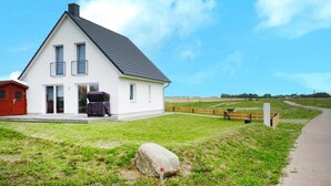 Une maison blanche à deux étages, avec un toit foncé, un barbecue abrité et un grand rocher au premier plan.