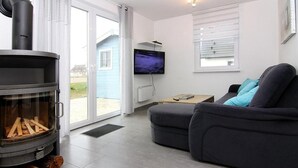 Un salon moderne avec une cheminée, un canapé, un téléviseur et une vue sur l’extérieur.
