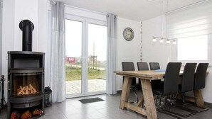 Un salon moderne doté d’un poêle à bois, d’une table à manger avec des chaises et d’une grande fenêtre offrant une vue sur l’extérieur.