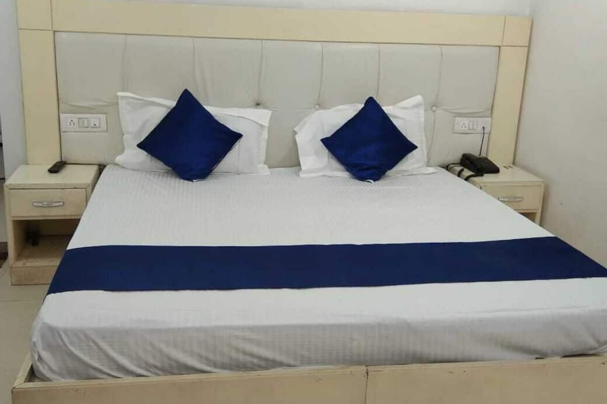 A bed with a white and blue bedspread, two blue pillows, and a beige headboard.