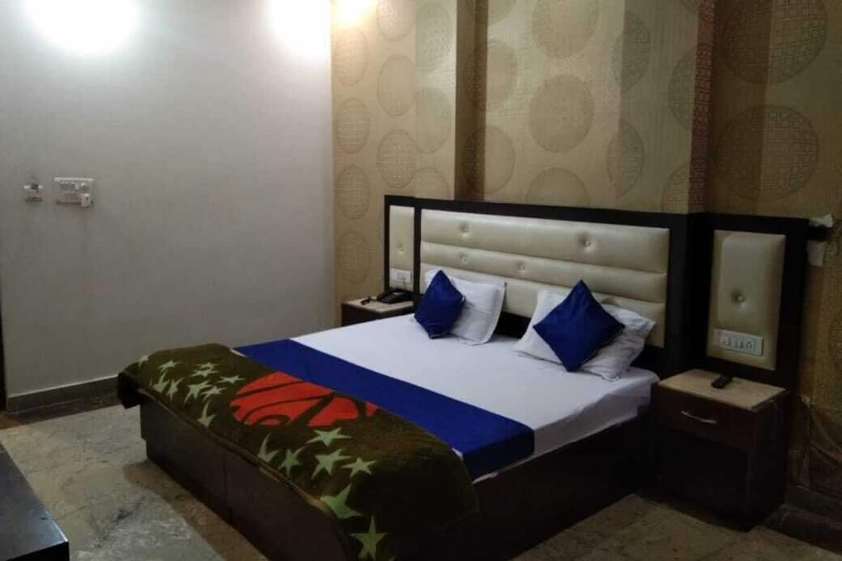 A hotel room with a bed, a nightstand, a bedside table, and a wall with a patterned wallpaper.