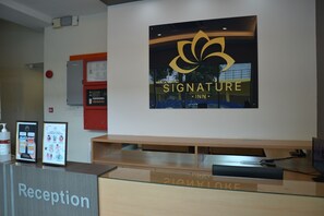 Un comptoir d’accueil orné du logo « Signature Inn », un espace d’accueil et un détecteur d’incendie fixé au mur.