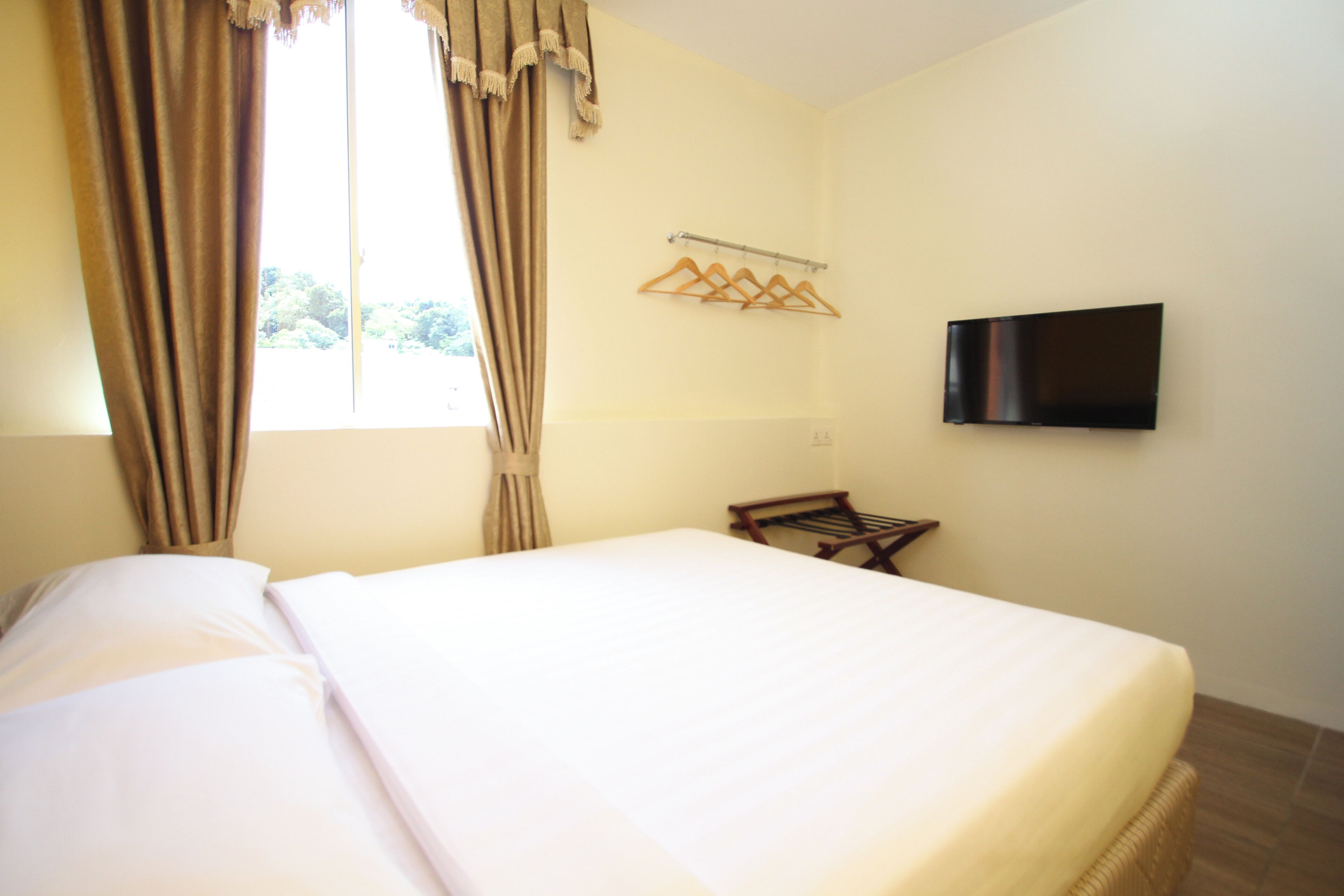 Habitación de hotel con una cama, televisor montado en la pared y una ventana con cortinas.