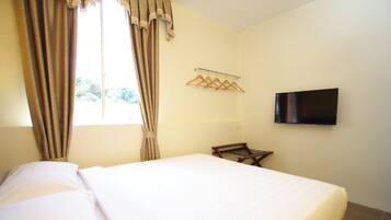 Habitación de hotel con una cama, televisor montado en la pared y una ventana con cortinas.