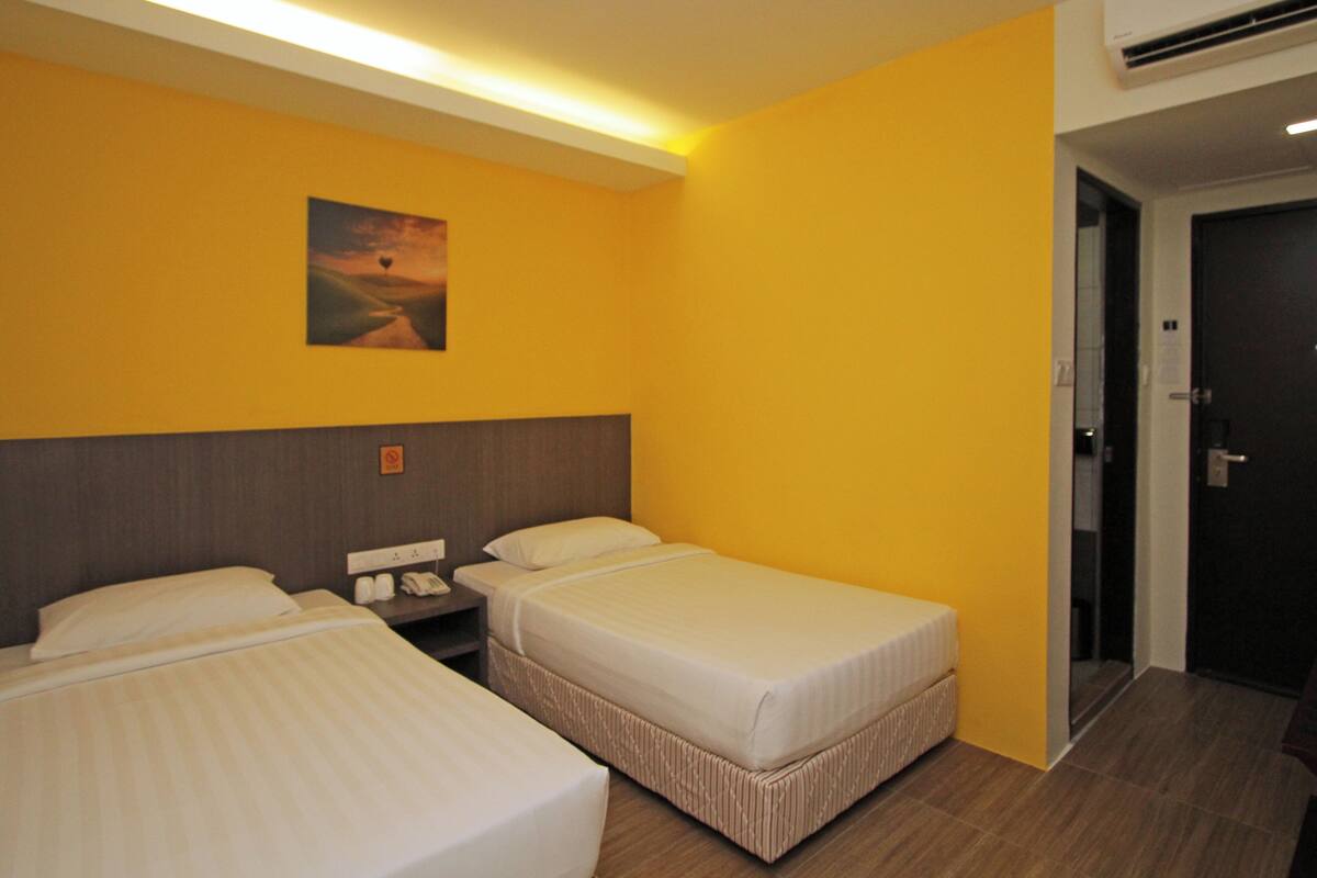 A hotel room with two beds, a nightstand, a painting on the wall, and a door.