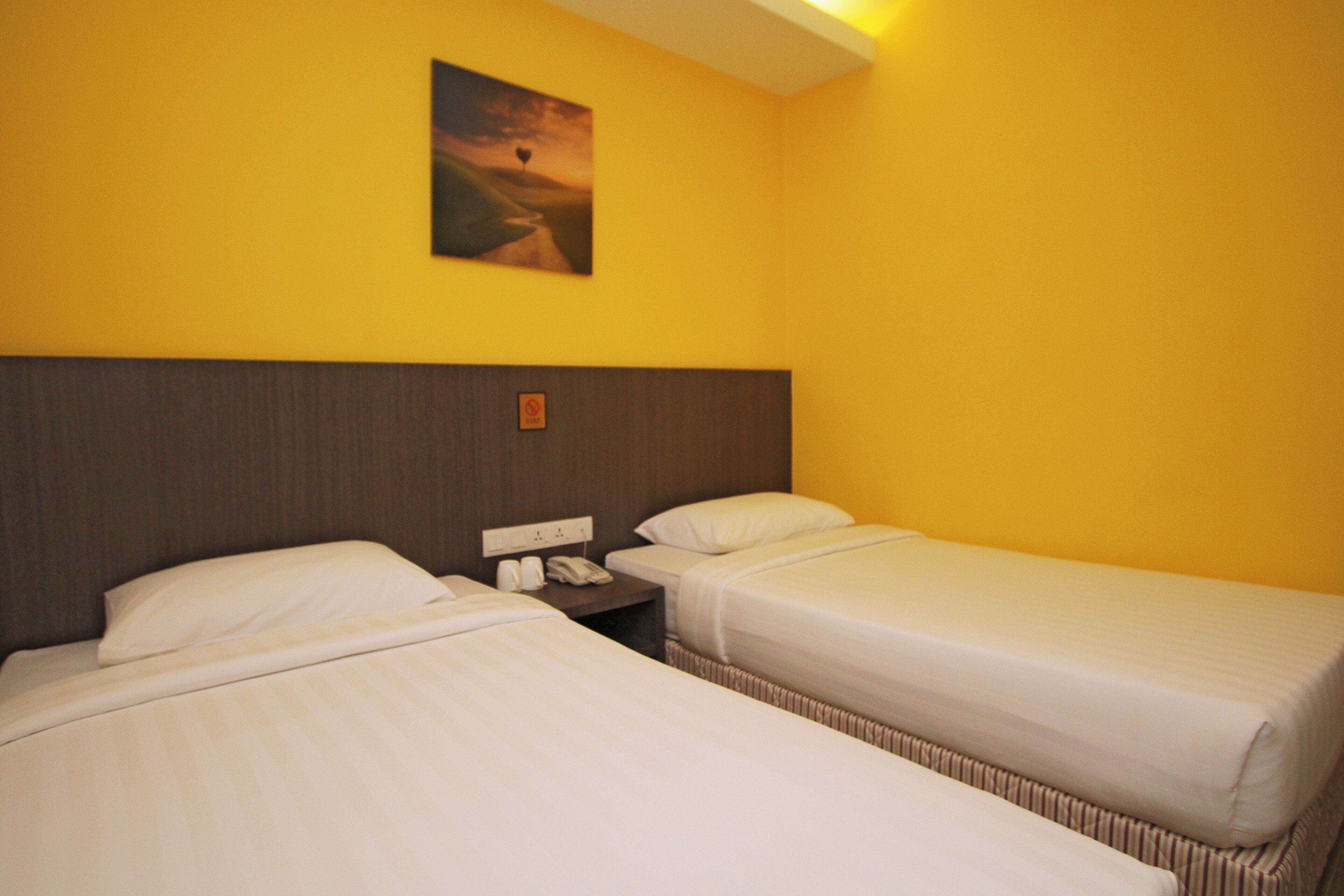 Quarto de hotel com duas camas, uma mesa de cabeceira com telefone e um quadro na parede.