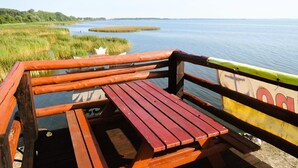 A wooden deck with benches overlooking a calm body of water, surrounded by grassy areas.