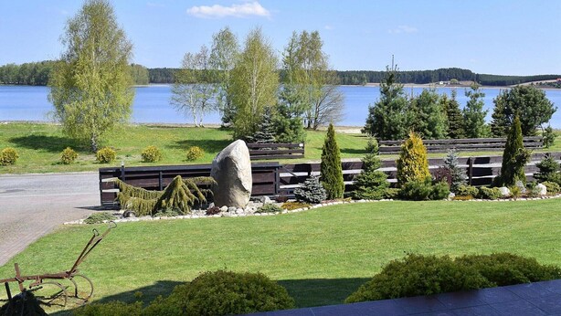 Une vue sur le lac, avec une terrasse en bois, un grand rocher et différents arbres.