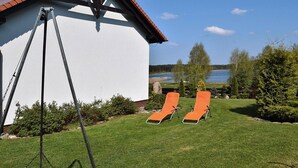 Un bâtiment blanc avec un toit rouge, une balançoire et deux chaises de jardin orange, le tout donnant sur un lac.