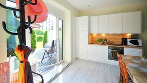 A modern kitchen with white cabinets, a microwave, and a sink. There is a dining table with chairs and a glass door leading to a patio area with a view of a building and greenery.
