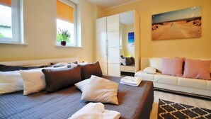 A hotel room with a bed, a sofa, a window with a plant, a painting on the wall, and a wardrobe.