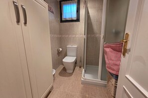 A bathroom with a toilet, shower, and a door with a striped towel hanging. - 15A06 Apartamento centrico en Llanes (Llanes)