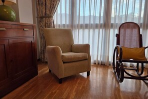 A room with a wooden floor, a beige armchair, a rocking chair, and a wooden cabinet. - 15A06 Apartamento centrico en Llanes (Llanes)