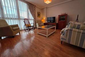 Un salon comprenant un canapé, des fauteuils, une table basse, un téléviseur et un meuble.