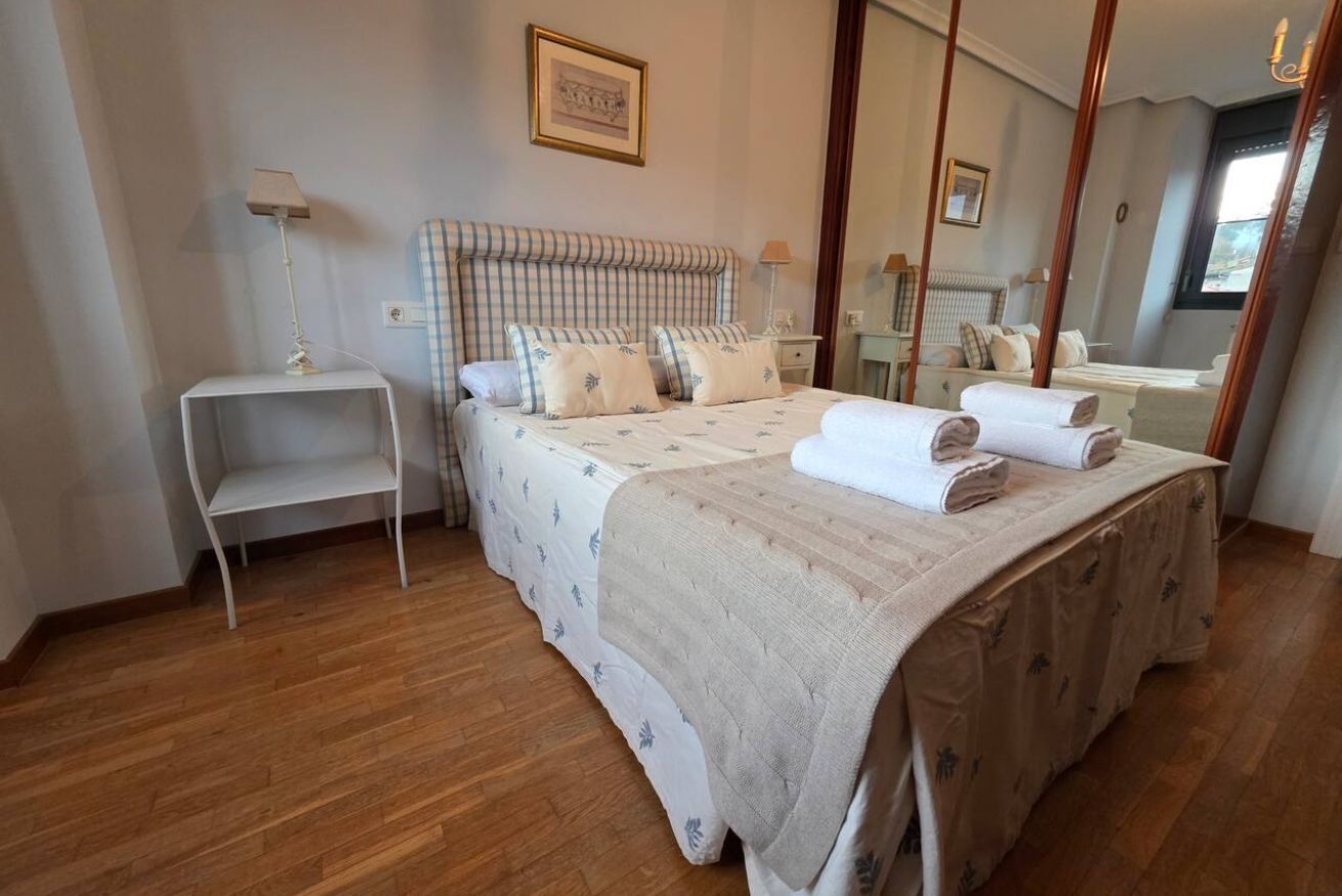 A bedroom with a large bed, bedside tables, a mirror, and a window.