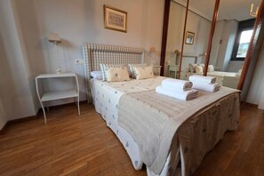 A bedroom with a large bed, bedside tables, a mirror, and a window. - 15A06 Apartamento centrico en Llanes (Llanes)