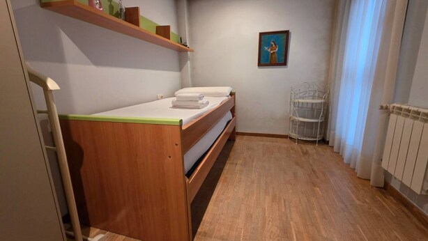 Ein kleiner Raum mit einem Holzbett, einem Regal mit Dekoration, einem gerahmten Bild an der Wand und einem Heizkörper.