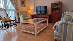 Ein Wohnzimmer mit Fernseher, einer Couch, einem Schaukelstuhl und einem Holzschrank.