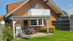 Ein zweistöckiges Haus mit einem Balkon, einer Terrasse mit Gartenmöbeln und einem umzäunten Hinterhof.