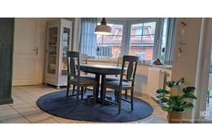 Un espace repas comprenant une table, des chaises, un luminaire suspendu, une fenêtre et une plante.