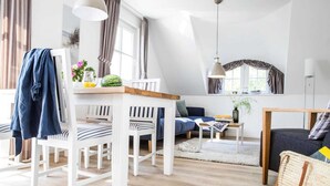 A modern living room with a dining area, featuring a white dining table, striped chairs, a sofa, and a coffee table. - Wohnung in Zingst nahe Ostseestrand (Zingst)