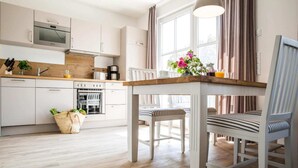 A modern kitchen with white cabinets, a wooden countertop, and a built-in oven. There is a dining table with striped chairs and a vase of flowers. - Wohnung in Zingst nahe Ostseestrand (Zingst)