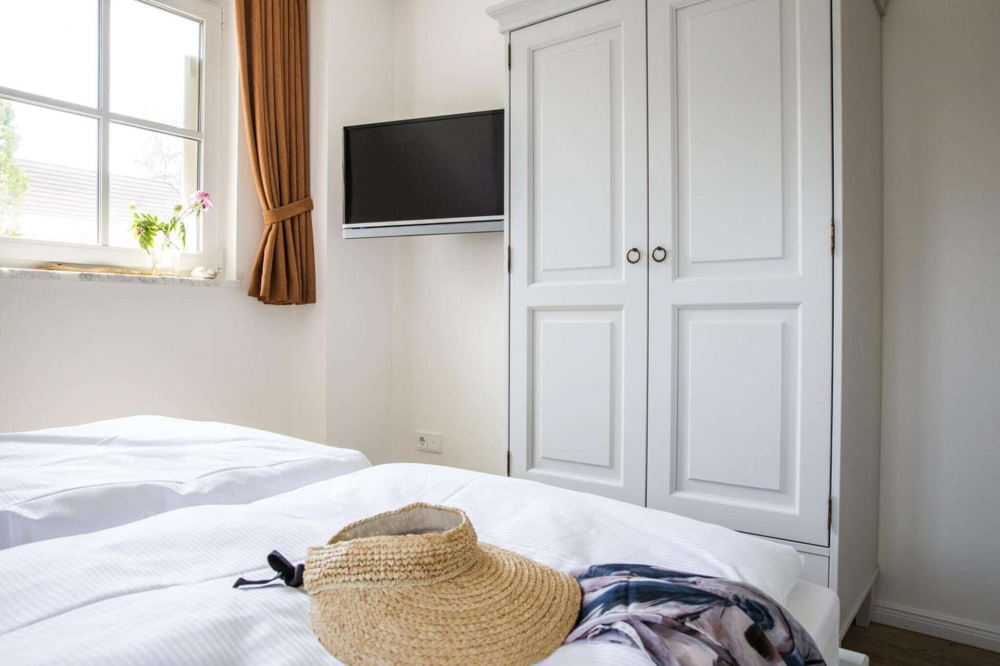 A hotel room with two beds, a TV mounted on the wall, and a wardrobe.