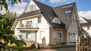 Una casa de dos pisos con balcón, paneles solares y entrada de ladrillo.
