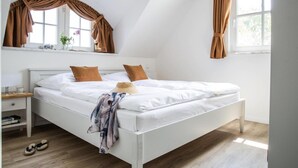 Un dormitorio con cama blanca, cortinas marrones, una ventana y una mesita de noche con libros.