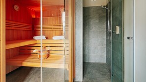 Een sauna met houten banken en een glazen scheiding, een doucheruimte met een glazen deur, en een betegelde vloer.