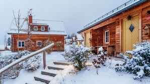 Een houten hutje met een gele deur, een trap naar de ingang en een besneeuwde omgeving.