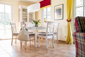 A dining area with a white table and chairs, a white cabinet, and a yellow curtain. - Luxushaus Bodden mit Schwimmbereich (Fuhlendorf)