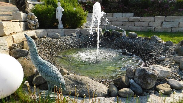 Un jardín con una fuente, rodeado de rocas y una estatua.